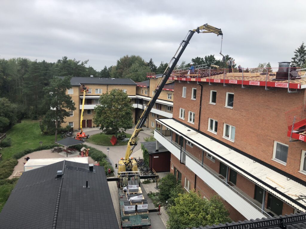 Lyftkran som lyfter upp material till medarebetare på taket för arbete med takbyte